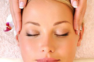 Woman's face with orchid flower in ear. Beautifully manicured hands visibly massaging womans temples. 